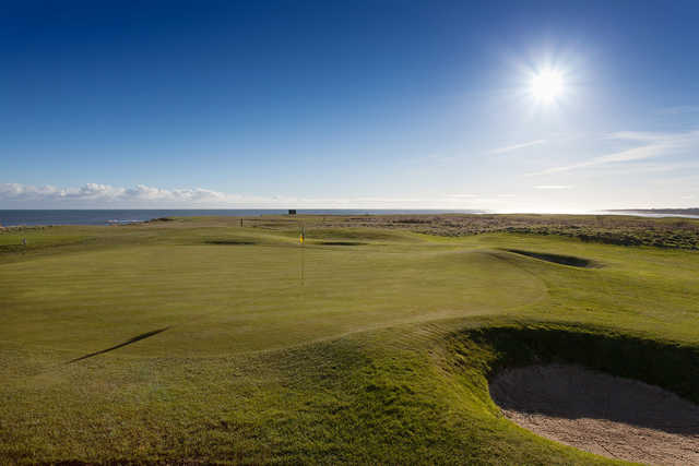 A sunny day view of a green with water in background at Seahouses Golf Club.