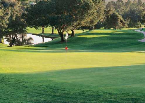 A sunny view of a green with narrow path on the right at Oaks North Golf Course