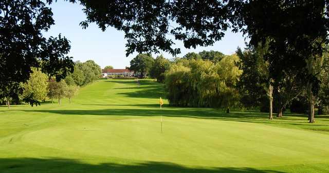 A sunny view of a green with the clubhouse in background at South Herts Golf Club.