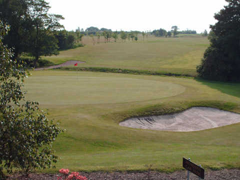 A view of a green guarded by sand traps at Mossock Hall Golf Club