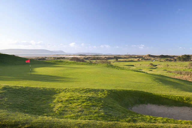 A sunny day view of a green with a bunker on the right side at Ashburnham Golf Club