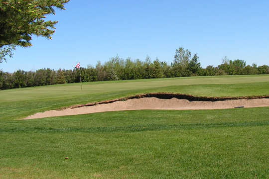 A view of a hole guarded by a bunker at Bow Island Golf Course
