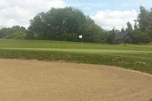 A view of a green protected by a bunker at Quinte Hills Golf Course