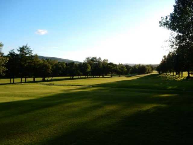 A scenic view of the fairway in the shadow of the trees at Glossop & District Golf Club