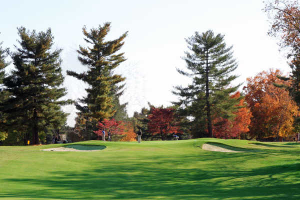 A sunny day view of a green flanked by tricky sand traps and surrounded by mature evergreens at Indian Hills Country Club
