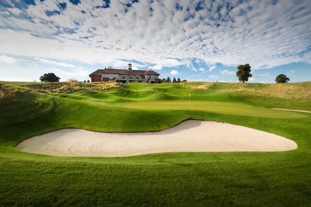 View of a bunkered green with the clubhouse in the background at The Oxfordshire Golf Club